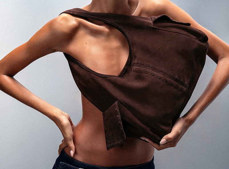 Person wearing a brown sleeveless top with a unique design on a gray background