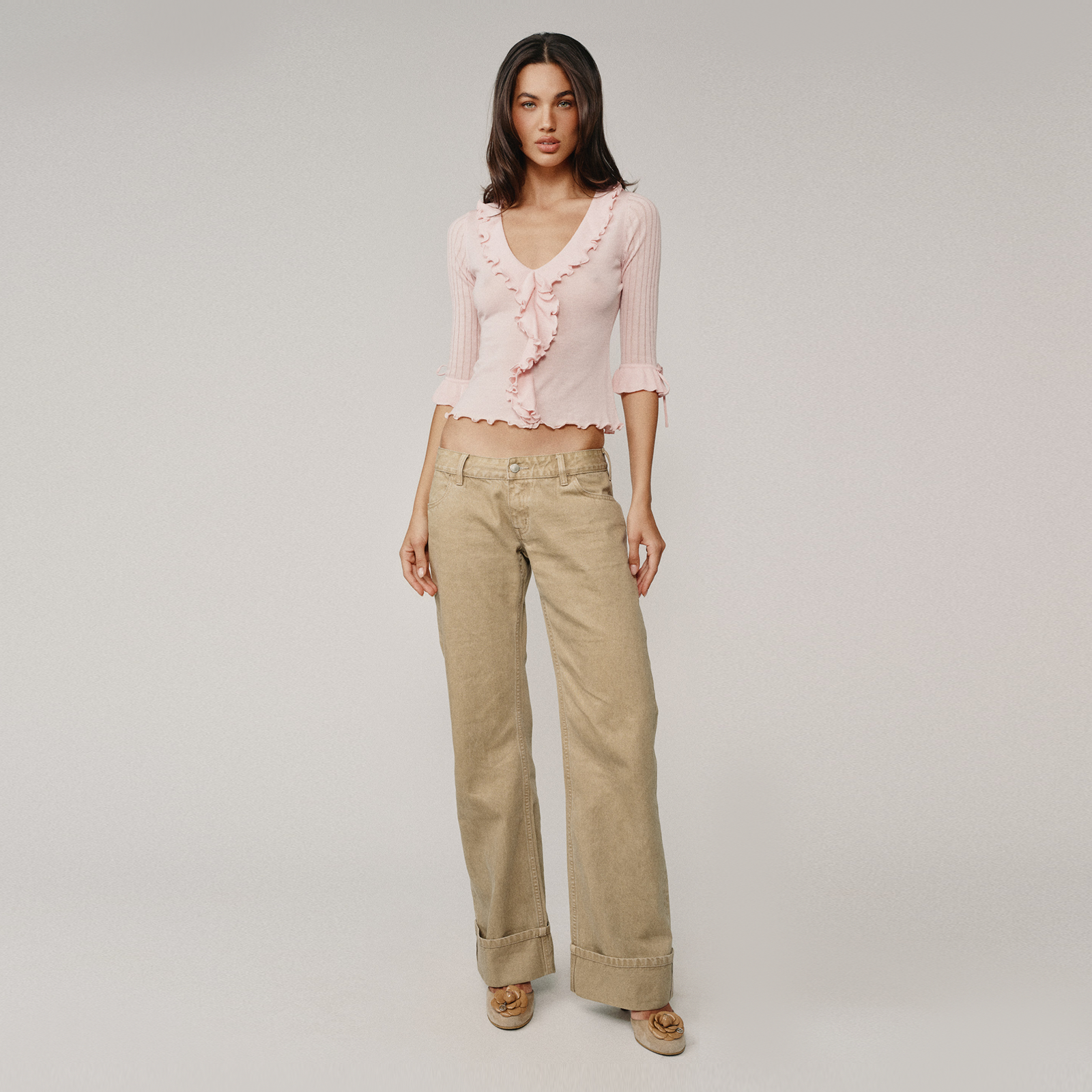 Woman wearing a pink top and beige pants on a plain background