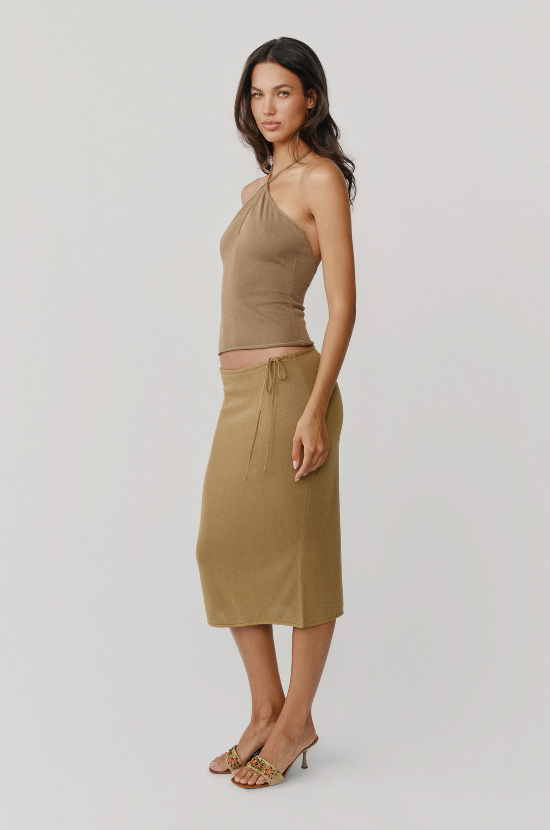 Olive midi skirt with a low-rise fit, adjustable side-tie waistband, and soft curved hemline.