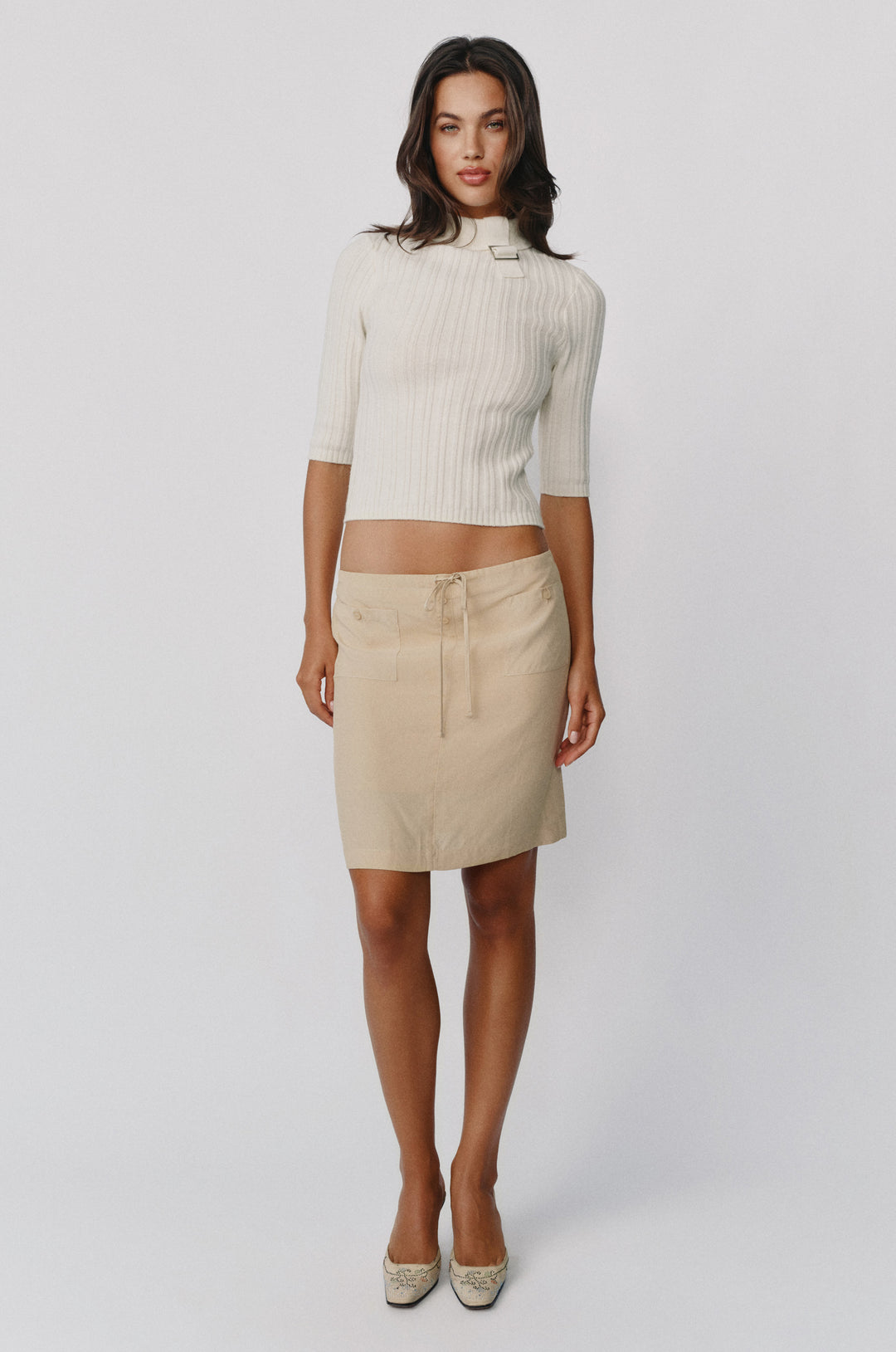 Beige low-rise Thea skirt with drawstring waist, front patch pockets, and button detailing worn with a ribbed top.