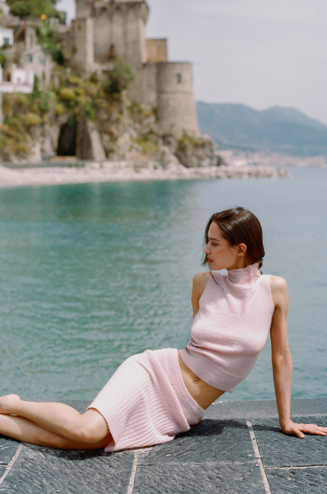 Pink knitted Trinity midi skirt with ribbed detailing, worn by a model by the sea.