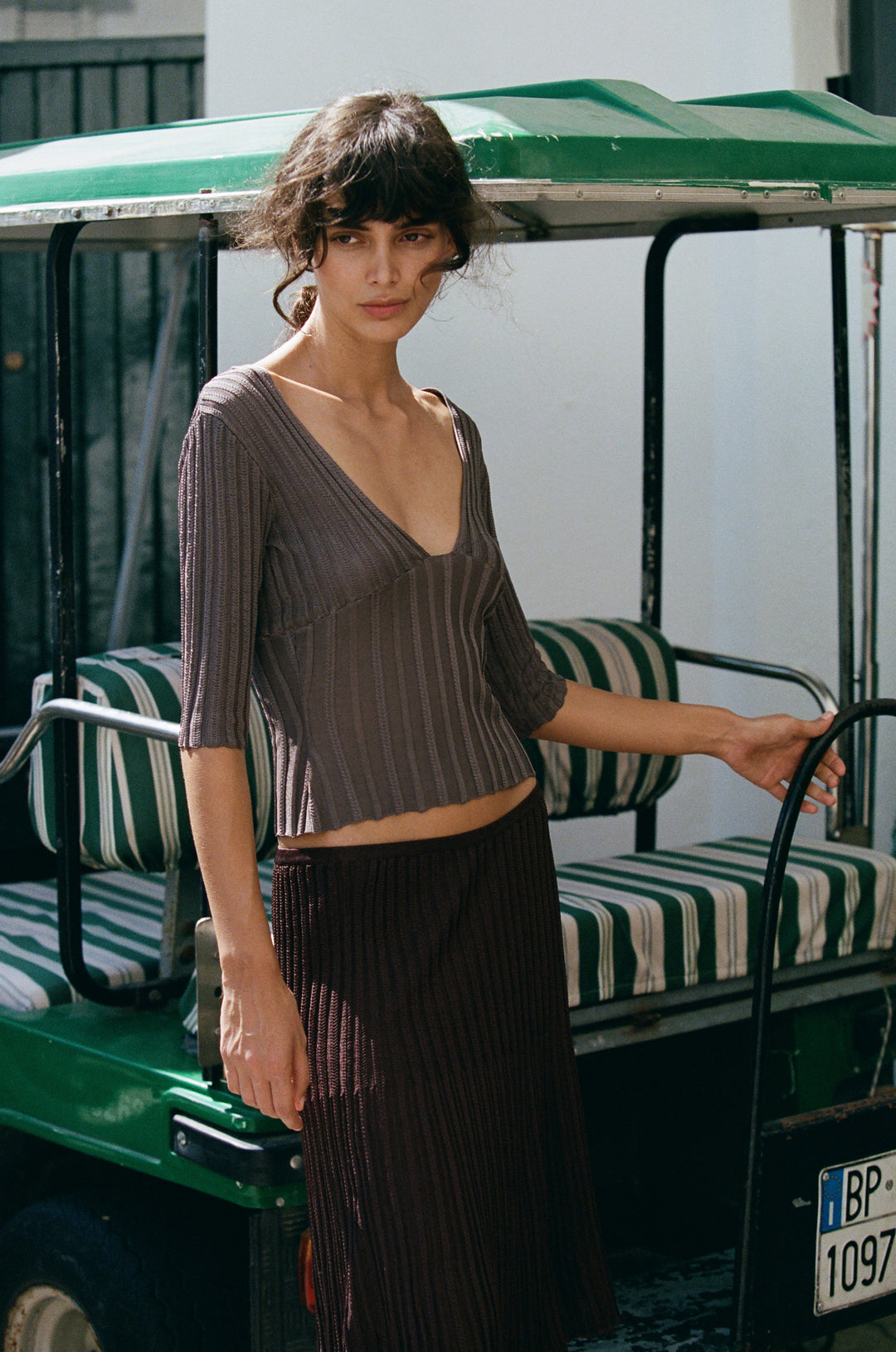 Smoke grey Veda top in ribbed knit with a V-neckline and half sleeves, worn with a matching dark brown ribbed skirt.