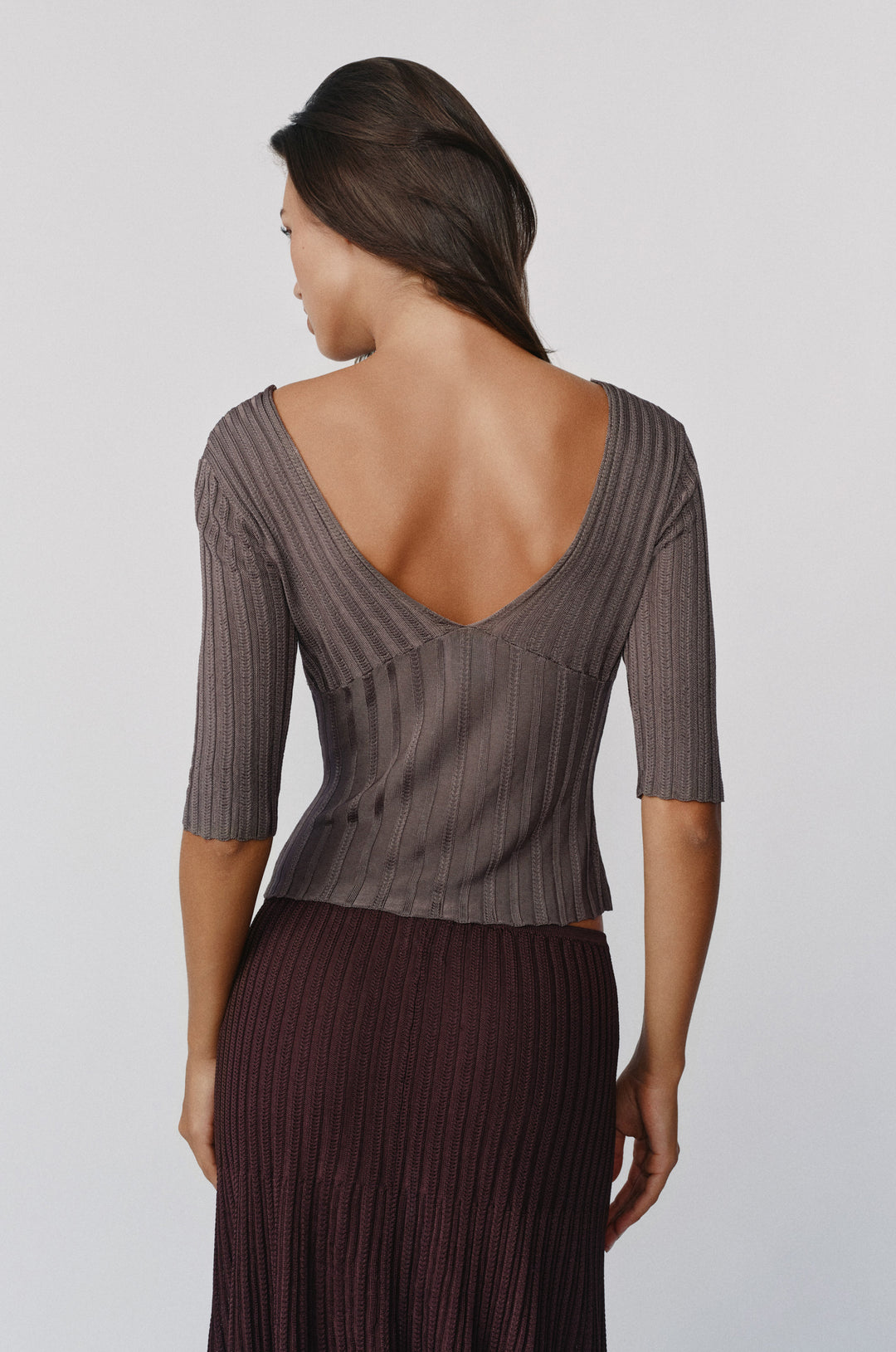 Smoke-colored ribbed-knit Veda top with half sleeves and a deep V-back neckline worn by a woman.