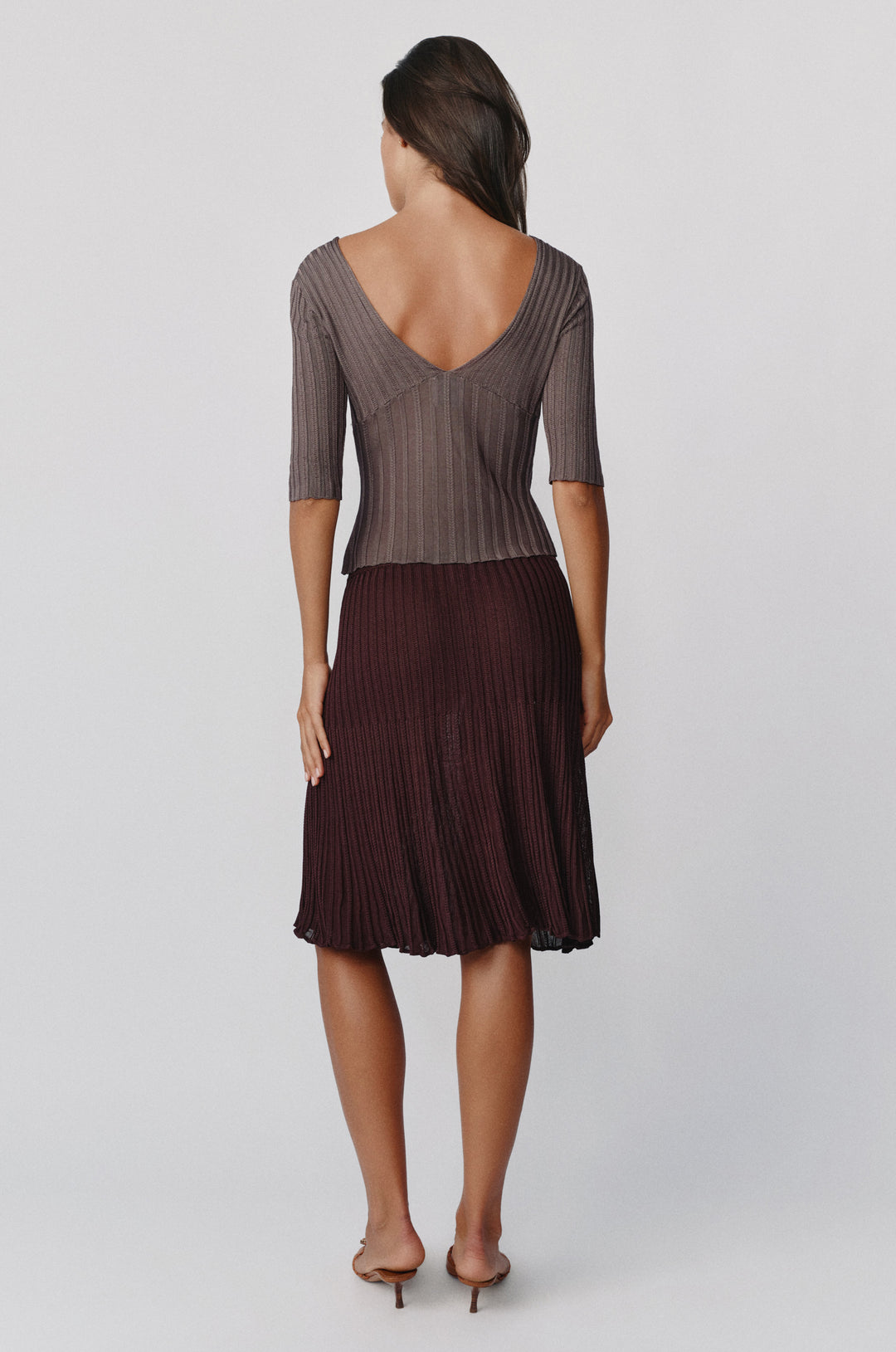 Back view of a smoke-colored ribbed-knit Veda top with half sleeves and a deep V-neckline paired with a dark skirt.