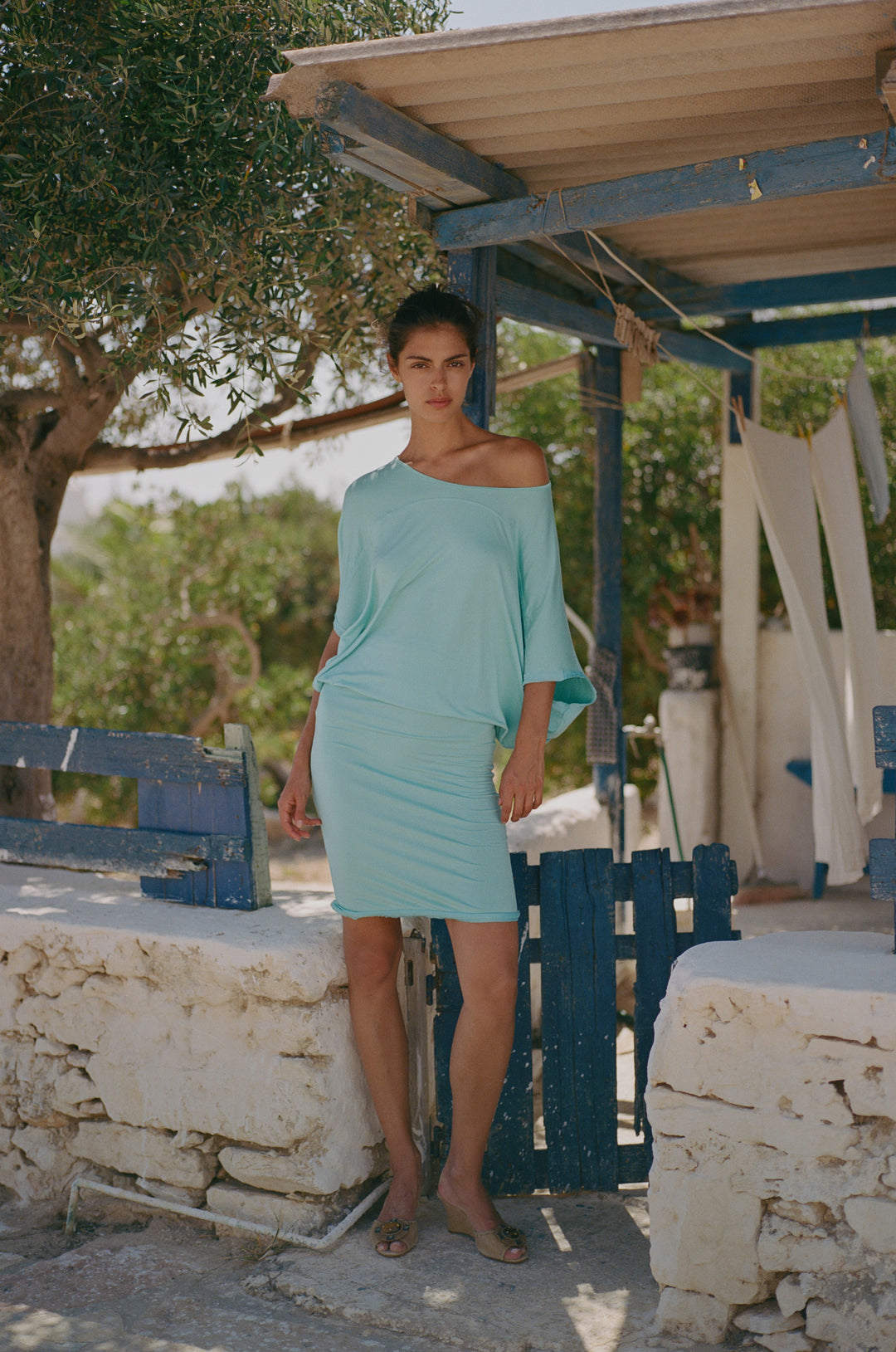 Aqua Vinnie dress featuring an off-the-shoulder relaxed neckline, fitted body, and raw edge hem worn outdoors.